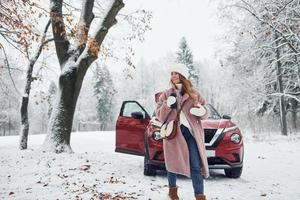 divirtiéndose. bella joven está al aire libre cerca de su automóvil rojo en invierno foto