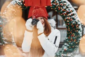 con cámara en manos. mujer joven feliz de pie al aire libre y celebrando las fiestas navideñas foto