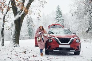 Having fun. Beautiful young woman is outdoors near her red automobile at winter time photo