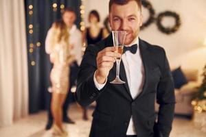 Man with glass of champagne is cheering. Group of people have a new year party indoors together photo