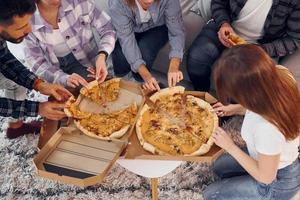 comiendo deliciosa pizza. grupo de amigos tienen una fiesta en el interior juntos foto