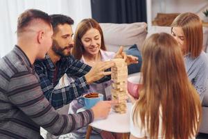 Playing wooden tower game. Group of friends have party indoors together photo