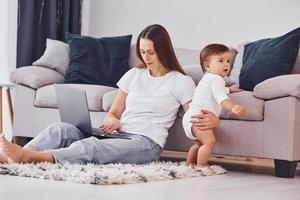 Woman working by using laptop. Mother with her little daughter is indoors at home together photo