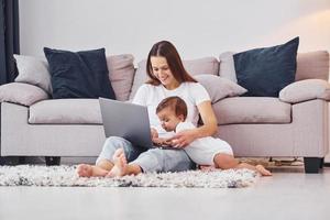 Using laptop. Mother with her little daughter is indoors at home together photo