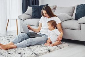 Silver colored laptop. Mother with her little daughter is indoors at home together photo