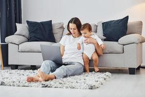 Silver colored laptop. Mother with her little daughter is indoors at home together photo