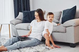 Silver colored laptop. Mother with her little daughter is indoors at home together photo