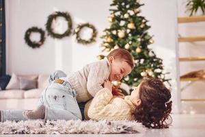 tumbado y jugando. el hermano y la hermana pequeños están juntos en la habitación decorada con navidad foto