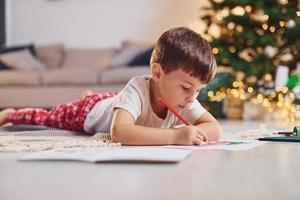 Drawing by using pencil. Little boy is in room with christmas tree is on the floor photo