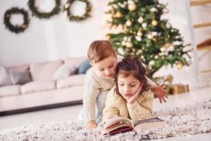 tumbado en el suelo. el hermano y la hermana pequeños están juntos en la habitación decorada con navidad foto