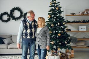 Standing near christmas tree. Senior man and woman is together at home photo