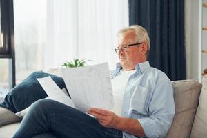 Holding two papers. Senior man in nice clothes is at home photo