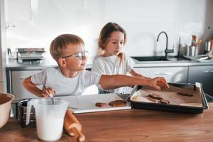 Holding cookie. Little boy and girl preparing Christmas sweets on the kitchen photo