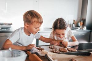 hermano y hermana ayudándose unos a otros. niño y niña preparando galletas navideñas en la cocina foto