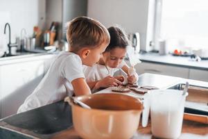 Brother and sister helping each other. Little boy and girl preparing Christmas cookies on the kitchen photo