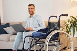 With laptop on the legs. Disabled man in wheelchair is at home photo