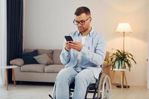 Using phone. Disabled man in wheelchair is at home photo