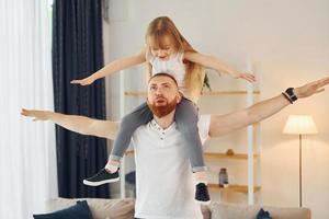 niña sentada sobre los hombros. padre con su pequeña hija está en casa juntos foto