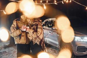 With warm drinks. Couple standing in the forest and celebrating New year photo