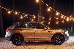 Side view. Modern silver colored automobile parked in forest with holiday decoration photo