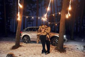 el coche está en el fondo. pareja de pie en el bosque y celebrando el año nuevo foto