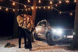 Standing near car. Couple is in the forest and celebrating New year photo