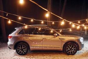 Side view. Modern silver colored automobile parked in forest with holiday decoration photo