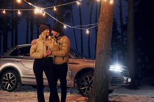 el coche está en el fondo. pareja de pie en el bosque y celebrando el año nuevo foto