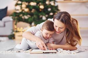 leyendo un libro juntos. madre con su pequeña hija está adentro en casa juntos foto