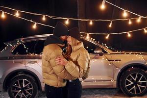 con coche moderno detrás. pareja de pie en el bosque y celebrando el año nuevo foto