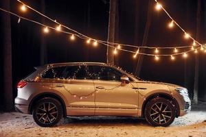 Side view. Modern silver colored automobile parked in forest with holiday decoration photo