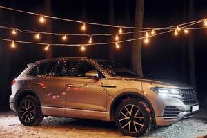 Modern silver colored automobile parked in forest with holiday decoration photo