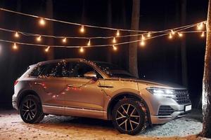 Modern silver colored automobile parked in forest with holiday decoration photo