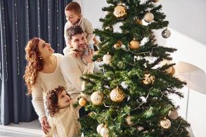 Decorating christmas tree. Family celebrating new year with their children at home photo