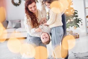 Standing in the domestic room and holding boy in hands. Family celebrating new year with their children at home photo