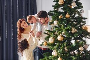 Decorating christmas tree. Family celebrating new year with their children at home photo