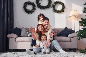 sentado cerca del sofá. familia celebrando el año nuevo con sus hijos en casa foto