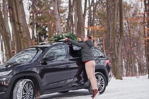 Preparing for the weekend. Man with little green fir is outdoors near his car. Conception of holidays photo