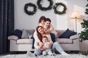 sentado cerca del sofá. familia celebrando el año nuevo con sus hijos en casa foto