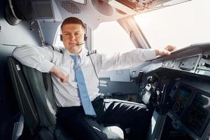 Pilot in formal wear sits in the cockpit and controls airplane photo