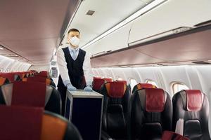 Steward in uniform is walks with luggage inside of airplane photo