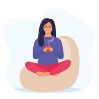 Young woman sitting on bean bag in a Lotus pose and holds a mug of hot drink in her hands. Cozy rest and relaxation concept. Vector illustration.