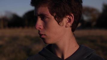 jeune homme, adolescent se tient dans le champ en regardant le coucher du soleil video