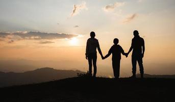 silueta de familia al aire libre al atardecer, familia feliz relajarse en la montaña. foto