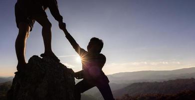 silueta de mano amiga entre dos escaladores. Pareja de senderismo se ayuda mutuamente a la silueta en las montañas con luz solar. los hombres que ayudan a sacar a la gente de los altos acantilados foto