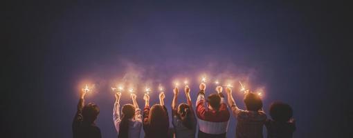 grupo de jóvenes amigos disfrutan con la quema de bengalas en las manos juntos foto
