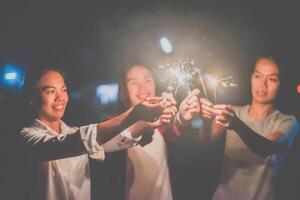 Young woman playing fireworks burning sparklers with friends photo