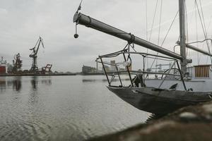 Front part of the mooring yacht in Docks on the Martwa Wisla in Poland city of Gdansk with port cranes in background during the cloudy autumn morning photo