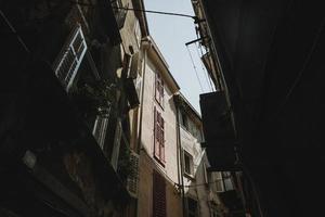 vista de abajo hacia arriba a las cimas de los edificios antiguos iluminados por el sol de verano desde la sombra de la calle en la ciudad histórica de piran en eslovenia con el cielo azul claro arriba foto