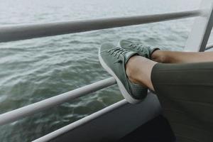 Detail of womans legs in green sneakers and green skirt resting on the railing of the ferry photo